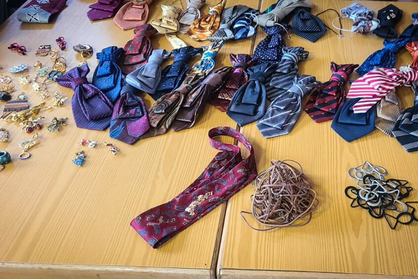 auf dem Tisch liegen zahlreiche Krawatten und Krewetten, dazu kleine Anstecker zum verzieren